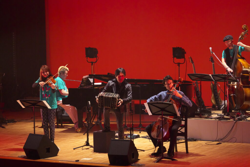 リベルタンゴは真っ赤な背景の前に バンドネオン小松良太 チェリスト松本しん バイオリニストの3人が奏でます